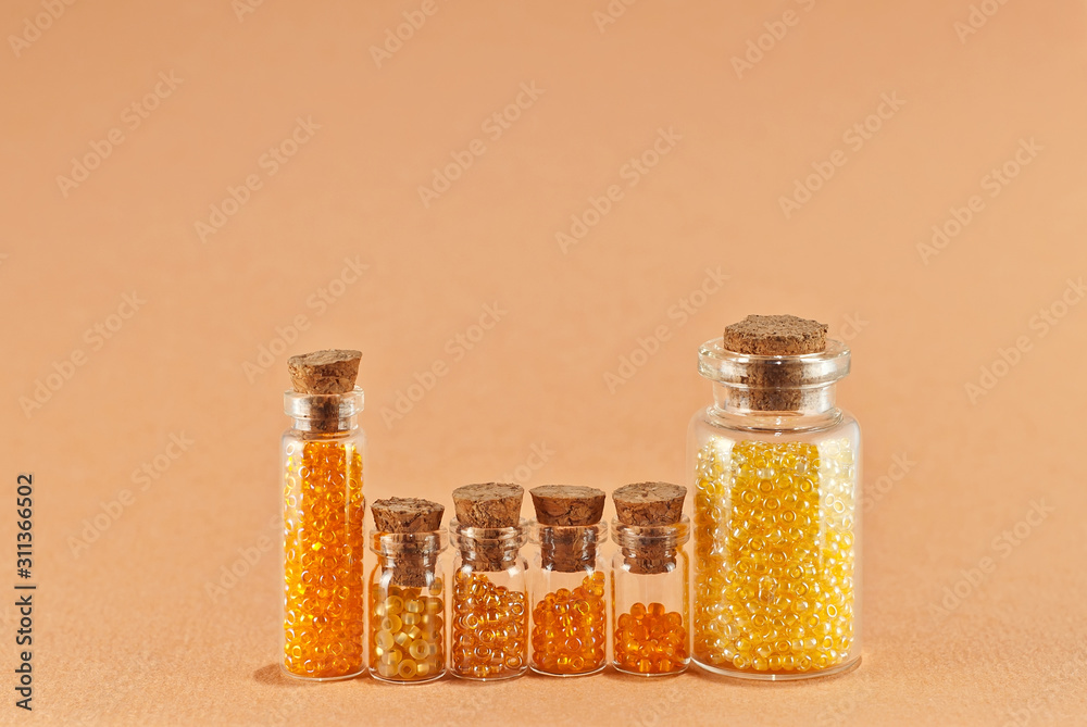 Yellow and red beads in glass jars on bright orange background. Beads in a transparent container with a wooden cork. The concept of orderliness, balance and chaos. Yellow and red beads in glass jars on bright orange background. Beads in a transparent container with a wooden cork. The concept of orderliness, balance and chaos.