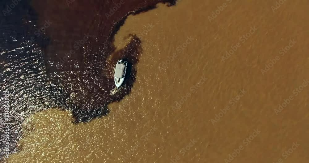 Aerial view over the white boat standing on the border of the confluence between the dark Rio Negro and the pale sandy-colored Amazon River upper flow, referred as the Solimões River. Manaus. Brazil