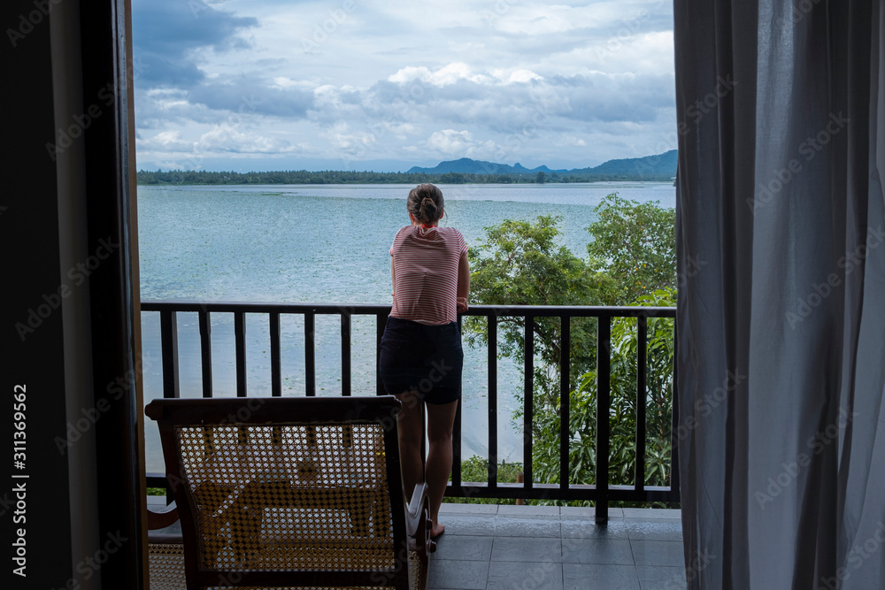 Woman leaning on a balcony cealing looking over Tissa lake, Sri Lanka