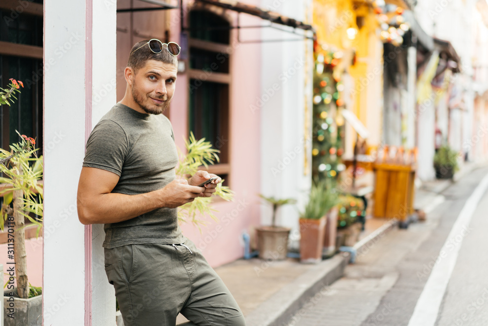 Portrait of a young man in green clothes, outdoors, holding a mobile phone and smiling. Communication in social networks. Portrait of a young man in green clothes, outdoors, holding a mobile phone and smiling. Communication in social networks.