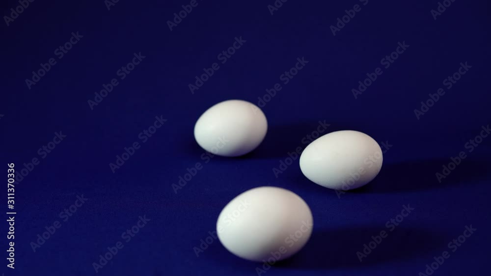 The shadows of three white eggs move clockwise on a blue background, a minimalist Easter background with space for text.
