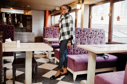 African woman in checkered cape posed at cafe.