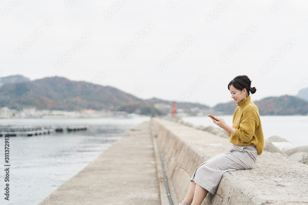海でスマートフォンを使う女性