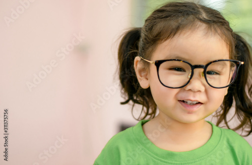 An Asian kindergarten girl is standing wearing glasses.