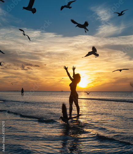 Silhouette of a happy young woman with raised arms stands against the beautiful sea beach at sunset Holbox island Mexico
