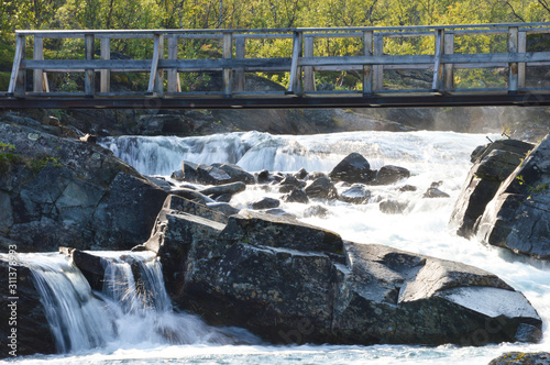 Bridge over wild river and rapids near Kungsleden trail in Abisko national Park, Sweden photo