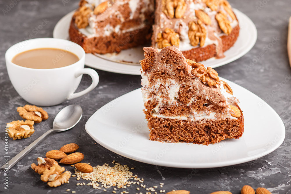 Homemade cake with milk cream, cocoa, almond, hazelnut on a black concrete background and a cup of coffee. Side view. Homemade cake with milk cream, cocoa, almond, hazelnut on a black concrete background and a cup of coffee. Side view.