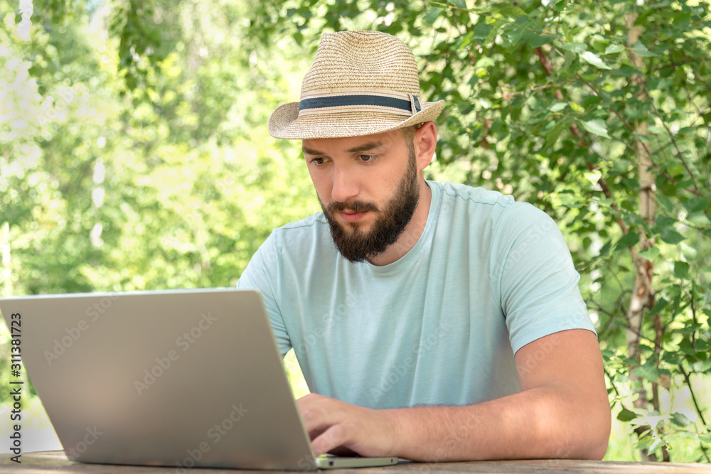 a man with a beard in a t-shirt is sitting at a laptop on the nature. concept of remote work and freedom