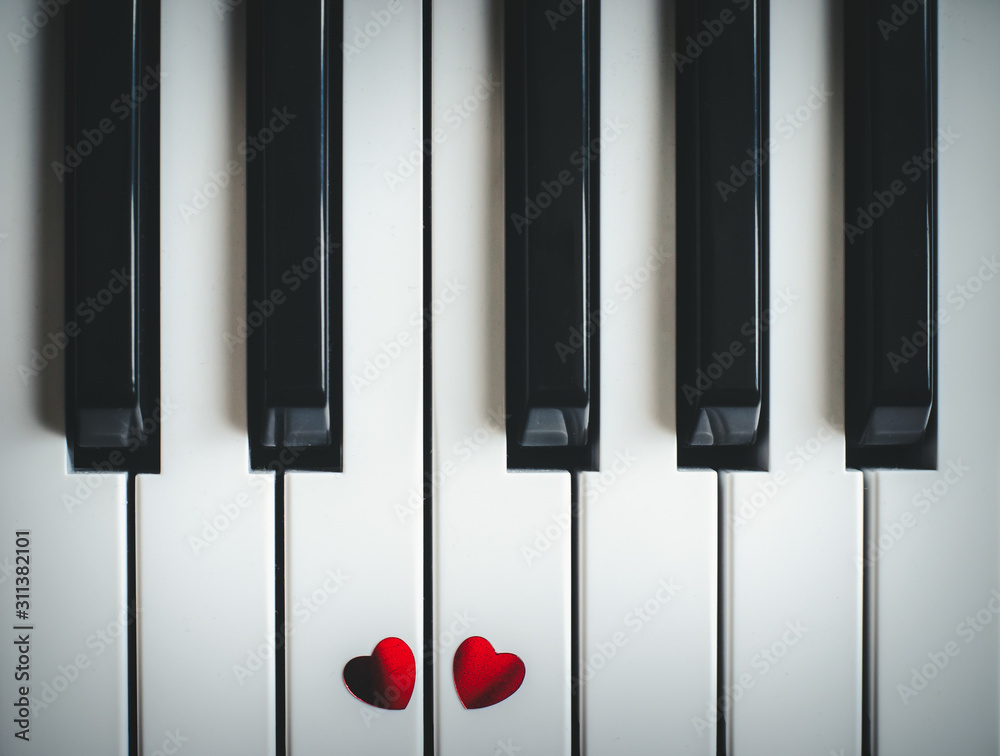 Naklejka premium Two small red hearts on the keyboard of classic piano close-up. Concept of love and romantic music