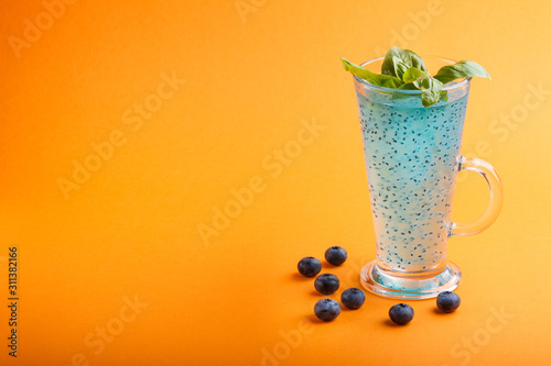 Glass of blueberry blue colored drink with basil seeds on orange background. Morninig, spring, healthy drink concept. Side view photo