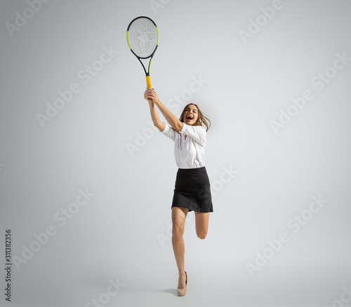 When it's getting you up. Woman in office clothes playing tennis on grey studio background. Businesswoman training in motion, action. Unusual look for sport, new activity. Sport, healthy lifestyle.