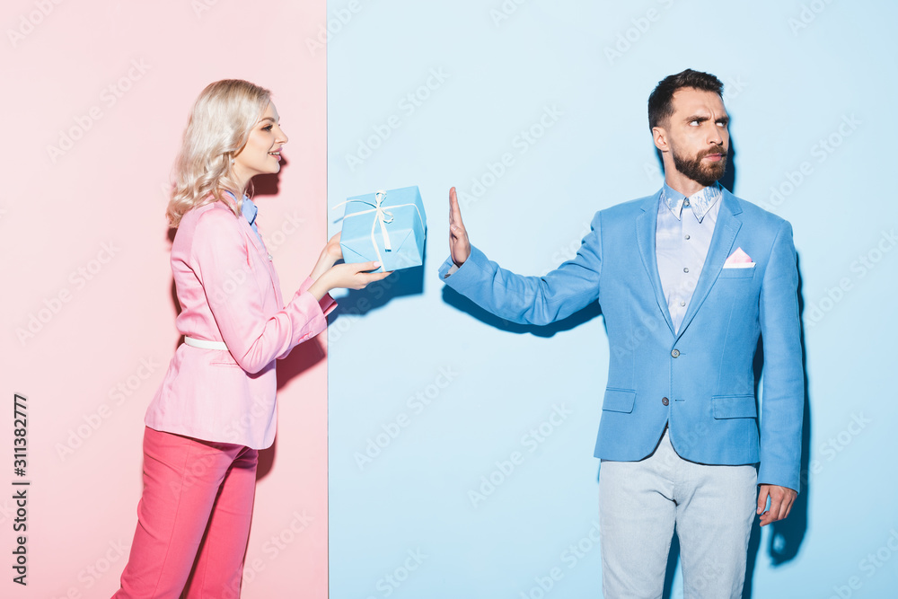 smiling woman giving gift to offended man on pink and blue background smiling woman giving gift to offended man on pink and blue background