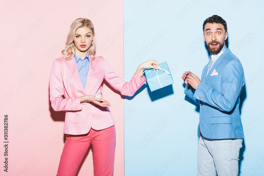 shocked woman holding gift and handsome man on pink and blue background shocked woman holding gift and handsome man on pink and blue background
