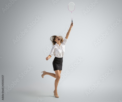 Time for fun and happiness. Woman in office clothes playing badminton on grey studio background. Businesswoman training in motion, action. Unusual look for sport, new activity. Sport, healthy