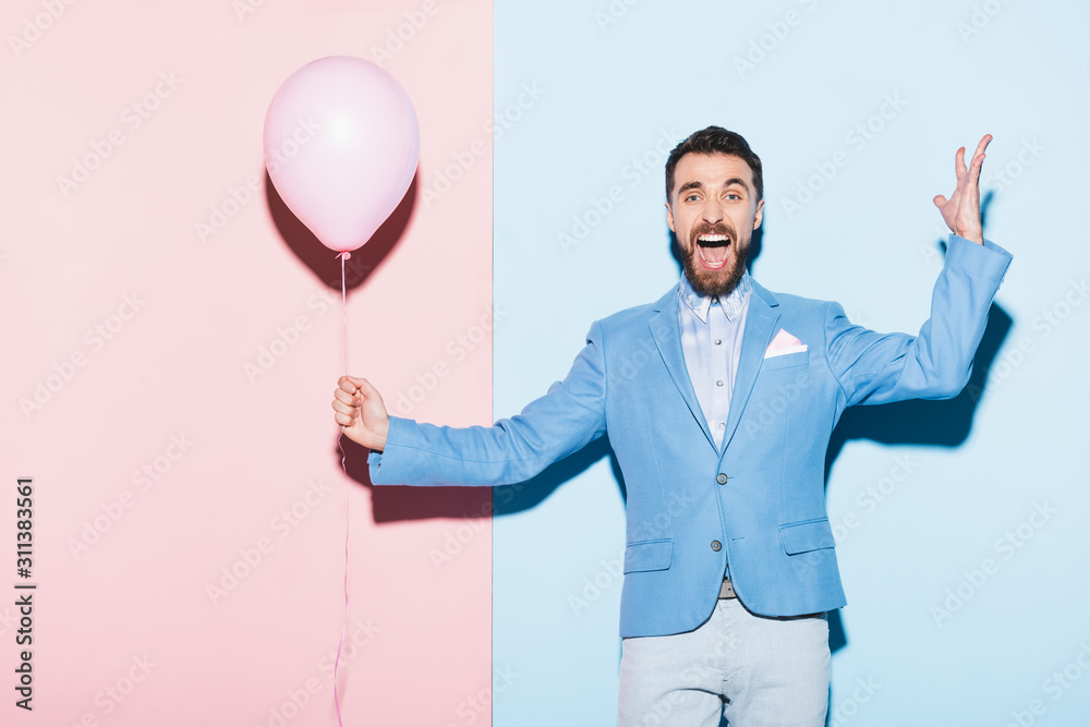 handsome and smiling man holding balloon on blue and pink background handsome and smiling man holding balloon on blue and pink background
