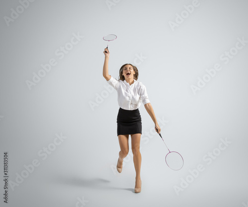 Movement. Woman in office clothes playing badminton with two racket on grey studio background. Businesswoman training in motion, action. Unusual look for sport, new activity. Sport, healthy lifestyle.