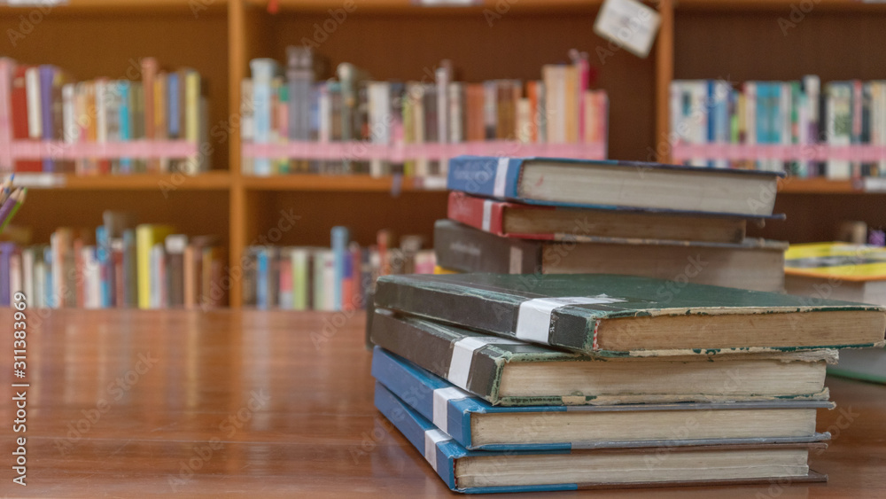 Books stack on table with book shelf background in library room