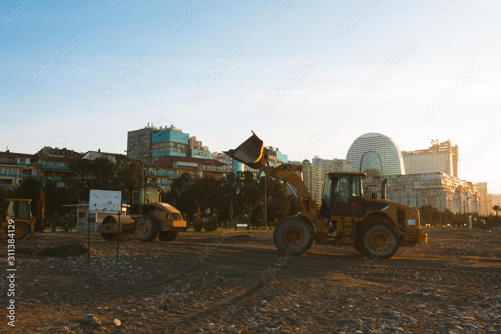 Fototapeta premium Excavator loads the excavation onto a truck (hydraulic)are heavy construction equipment consisting of an arrow,a bucket and a cabin on a rotating platform.On the beach with the sea and the setting sun