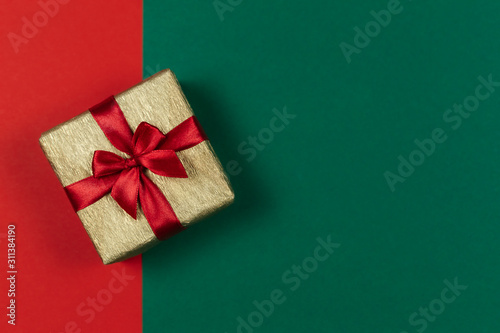 Golden gift box with red bow on the red and green background. Holiday concept. © Inna