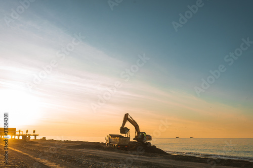 Excavator loads the excavation onto a truck (hydraulic)are heavy construction equipment consisting of an arrow,a bucket and a cabin on a rotating platform.On the beach with the sea and the setting sun