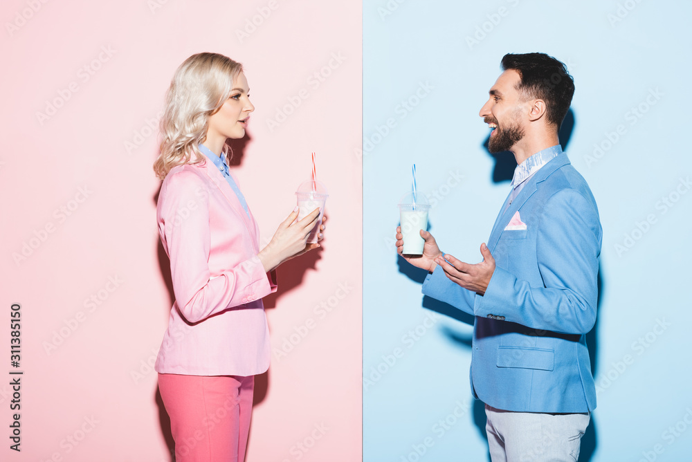 side view of attractive woman and smiling man holding cocktails on pink and blue background side view of attractive woman and smiling man holding cocktails on pink and blue background