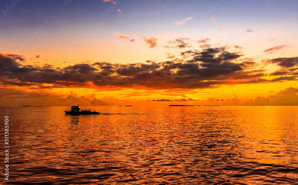 Amazing sunset at indian Ocean Golden Hour image near Maldive Island boat sailing along its journey beautiful orange and yellow color filled sky