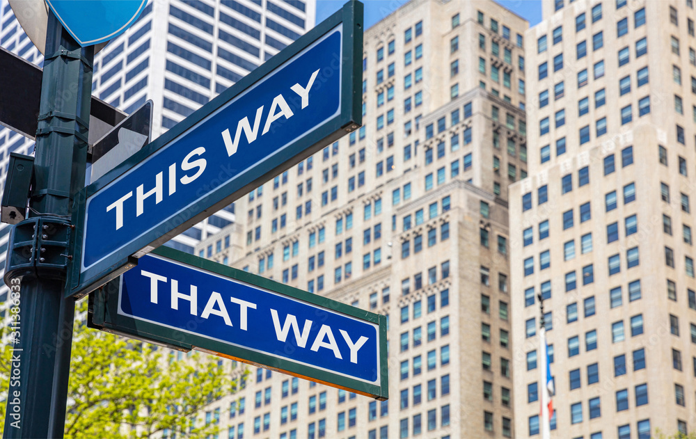 Fototapeta premium This way, that way crossroads street sign. Highrise buildings background,