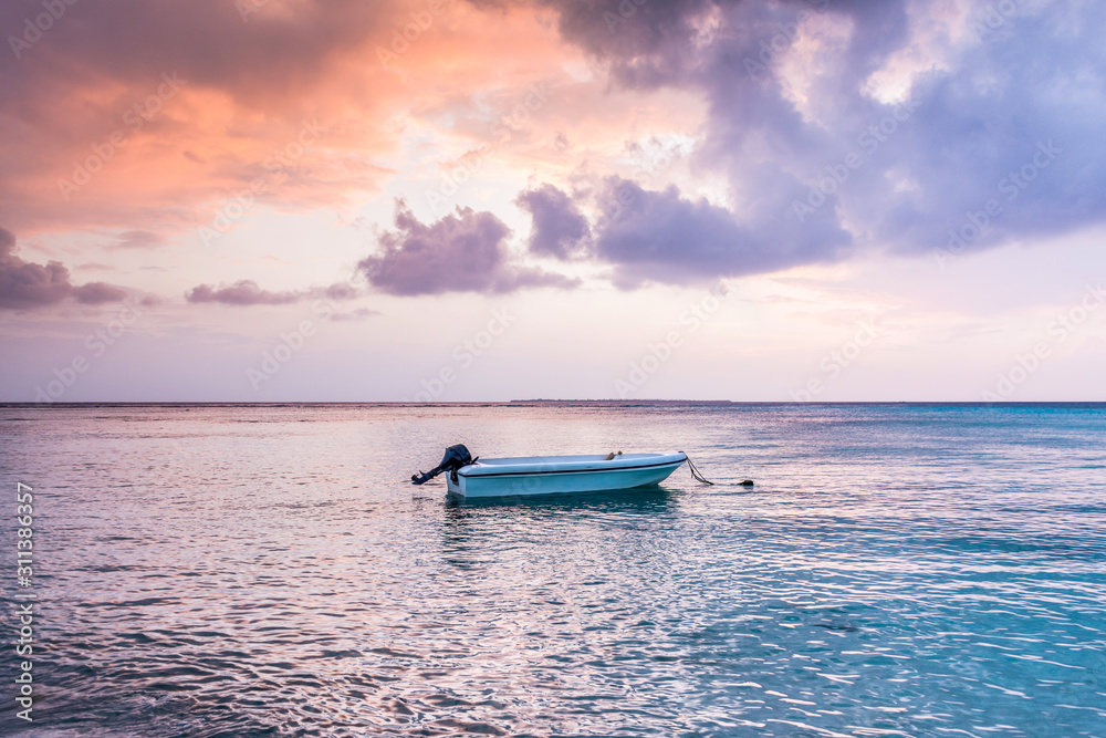 Naklejka premium Awesome Beach sunset at Maldives island Funadhoo colorful sky with alone boat at blue sea amazing nature scenery best place to travel in the world