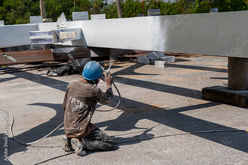 The painter is working to fireproof paint on steel structure with spray gun, at industrial factory.
