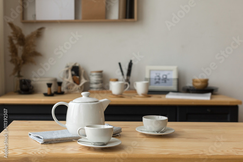Cute white teapot and white cups on table ready for tea drinking in light kitchen