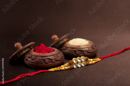 Raksha Bandhan background with an elegant Rakhi, Rice Grains and Kumkum. A traditional Indian wrist band which is a symbol of love between Brothers and Sisters.