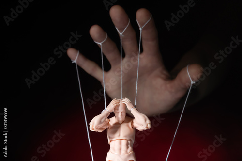 Concept of control. Marionette in human hand. Objects are colored on red and blue light. photo