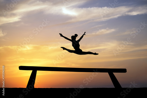 silhouette of female gymnast on balance beam in sunset