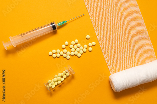 Syringe with pills for injection and vaccination on yellow background with bandage, concept of medecine