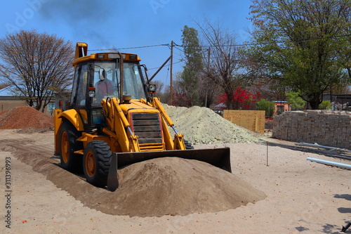 A backhoe pushing a pile of sand.This is a type of excavating equipment consisting of a tractor-like unit fitted with a loader-style shovel/bucket on the front and a backhoe on the back.