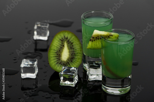 Green cocktail with kiwi in martini glasses with ice on a gray concrete background. Green cocktail with martini and kiwi on a gray background. Green cocktail with kiwi and martini.