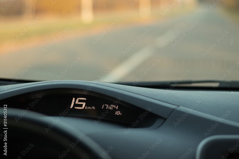 The dashboard of the car with a speed of 15 km / h on the speedometer, time, temperature and blured road on background; safe driving concept; speed limit; copy space; anomaly warm