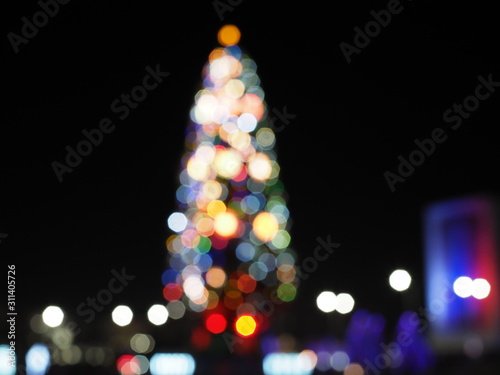 Christmas tree in the city square. Abstract dark blurry urban background.