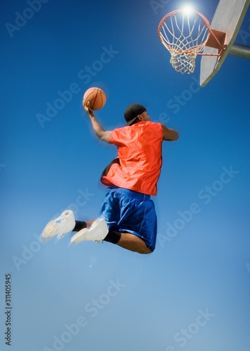 Man Dunking Basketball Into Hoop Against Blue Sky © moodboard