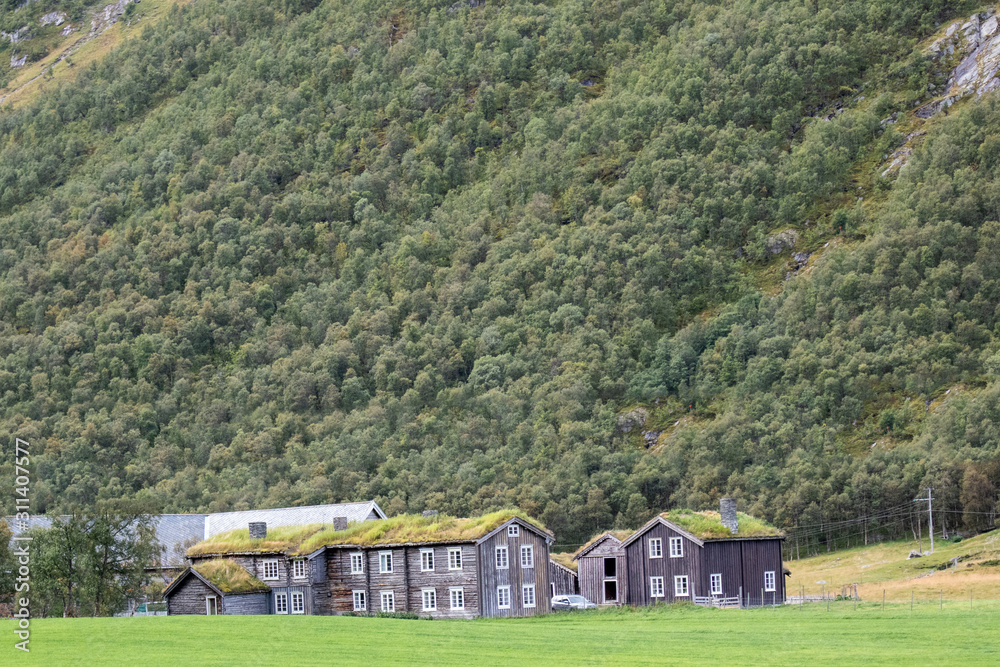 Wooden old traditional nordic houses with grass roofs in scenic landscape of mountains and pine forest Wooden old traditional nordic houses with grass roofs in scenic landscape of mountains and pine forest