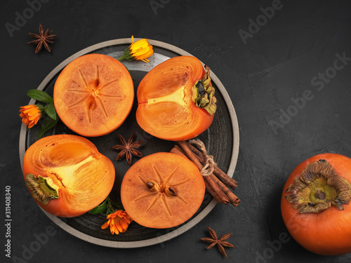 Delicious fresh persimmon fruit on a black background. Persimmon slices on a black plate. top view. Ingredients and spices for persimmon jam. photo