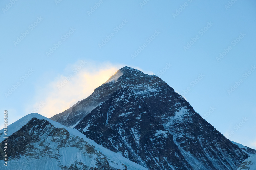 Summit of Everest mountain in Himalayas just before sunrise. Colorful snow is blown away from the top. View from the slope of Kala Patthar mountain. Theme of travel in Nepal. Clear blue sky.