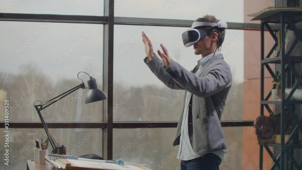male engineer in a virtual reality helmet near the large window with his hands imitates the work of the interface. Designing the future, the concept of virtual architecture and design, interface male engineer in a virtual reality helmet near the large window with his hands imitates the work of the interface. Designing the future, the concept of virtual architecture and design, interface