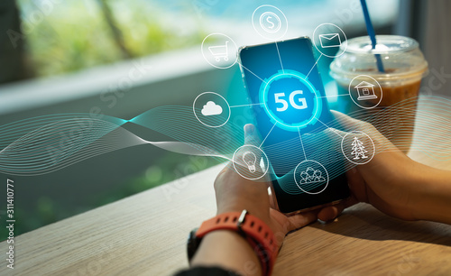 Close up of female hand holding a phone with a 5G hologram in coffee shop. 5G network wireless systems.The concept of 5G network, high-speed mobile Internet, new generation networks. photo
