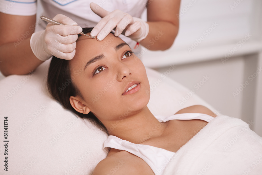 Attractive young Asian woman having blackhead removal procedure at cosmetology salon, copy space