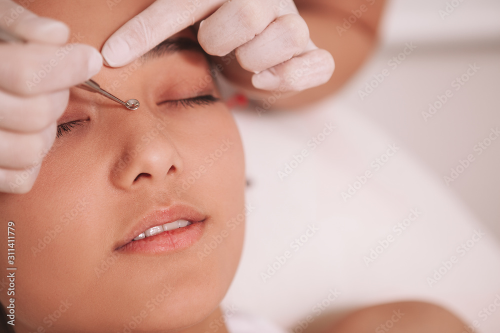 Cropped close up of a professional beautician removing blackheads on the nose of a female client. Skincare concept