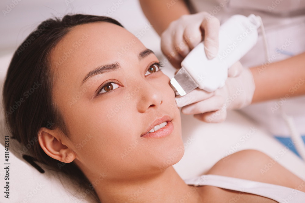 Beautiful young Asian woman receiving ultrasound cavitation treatment at beauty salon Beautiful young Asian woman receiving ultrasound cavitation treatment at beauty salon