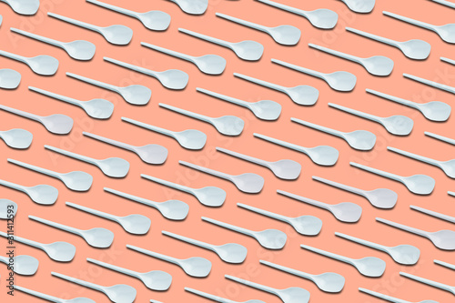 pattern of white disposable plastic spoons on bright background, top view, closeup, concept of big ecological problem