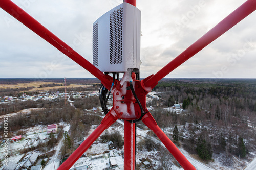 Red telecommunication tower or mast and remote electric tilt and remote radio unit with power and optic cables in winter day