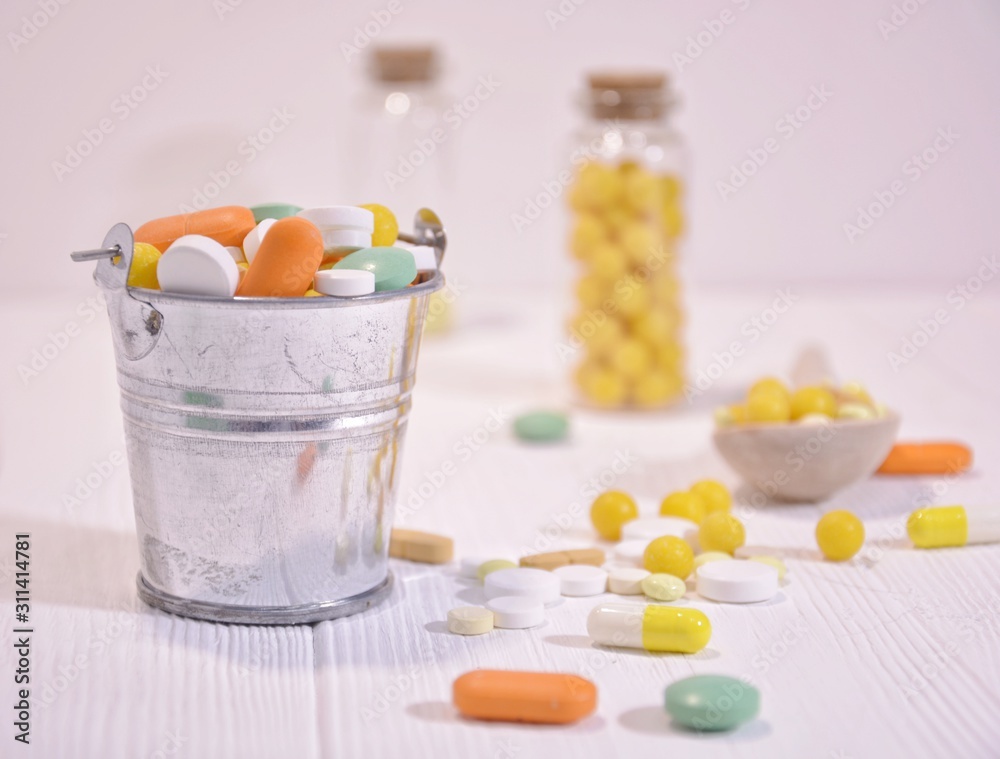 A bucket of multi-colored pills on a white wooden background with space for text. A bucket of multi-colored pills on a white wooden background with space for text.